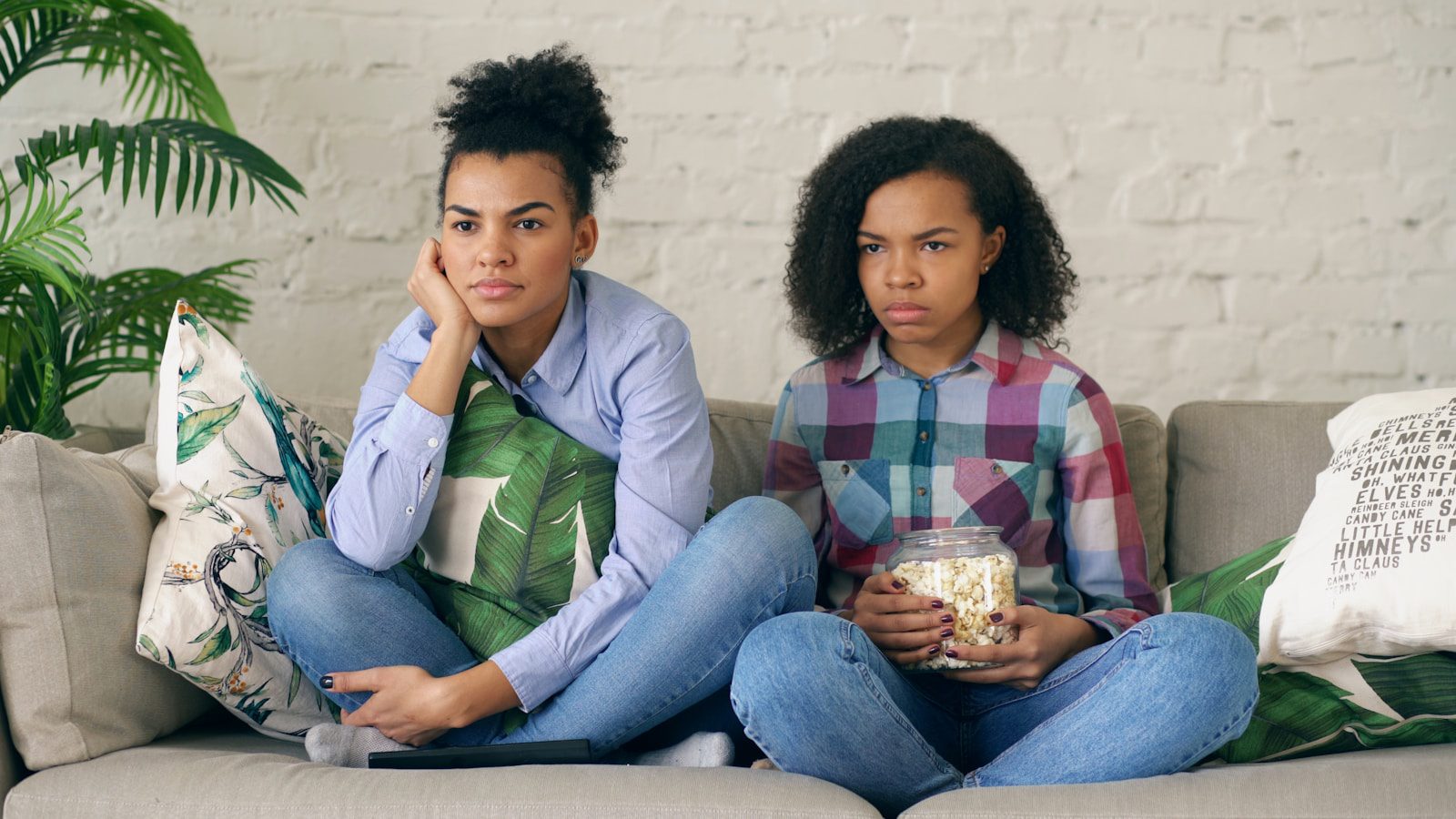 Two women sitting on a couch with popcorn.