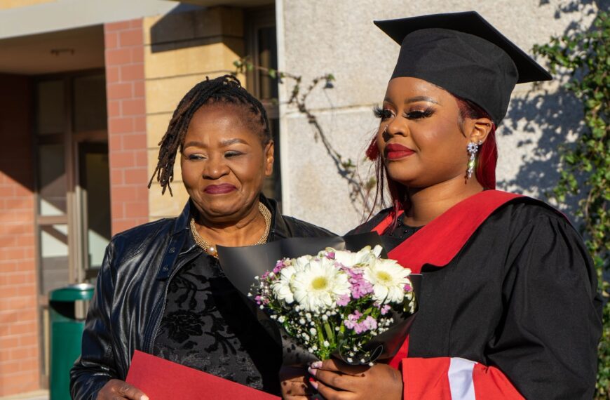 a woman in a graduation gown holding a bouquet of flowers