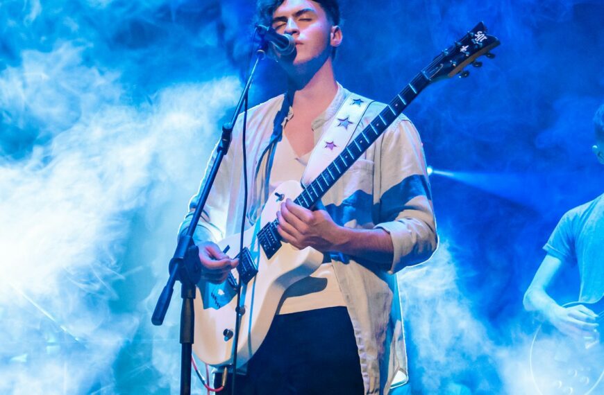 a man standing in front of a microphone while holding a guitar