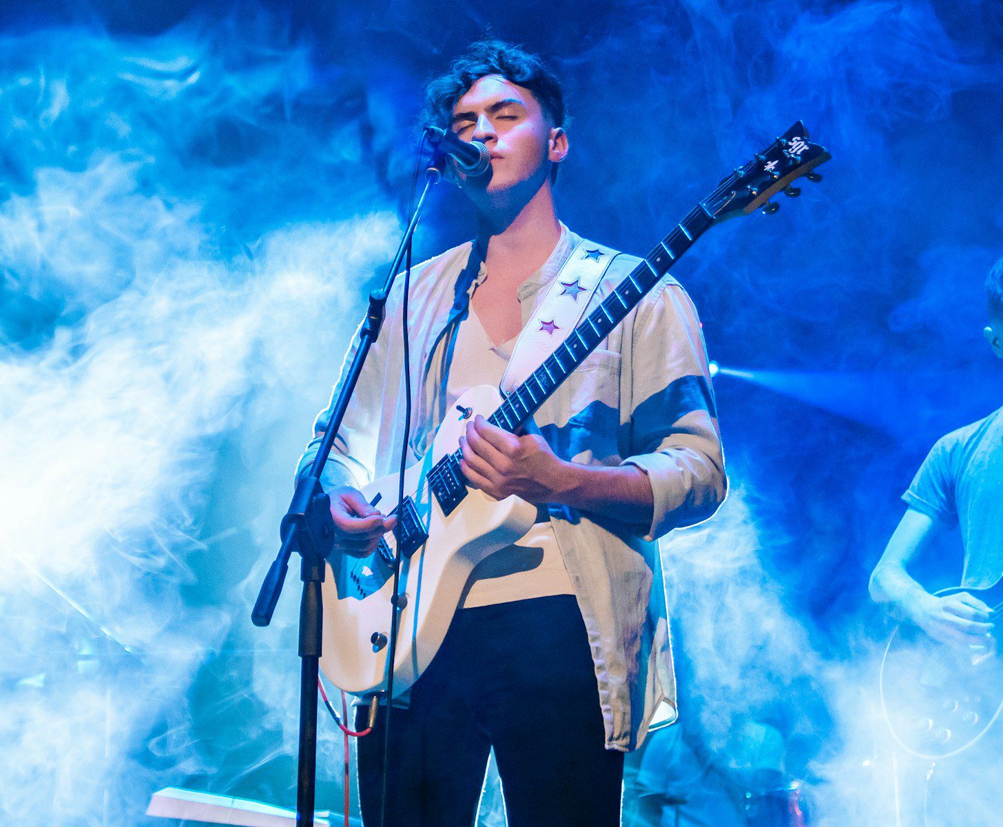 a man standing in front of a microphone while holding a guitar