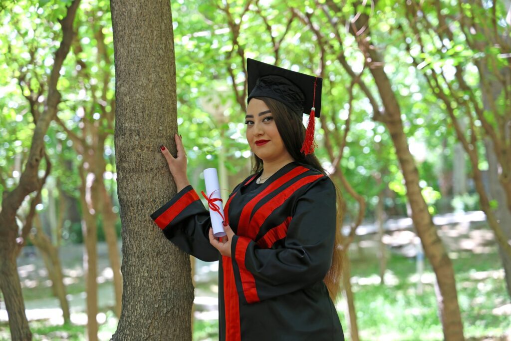 A graduate in cap and gown holds a diploma outdoors.