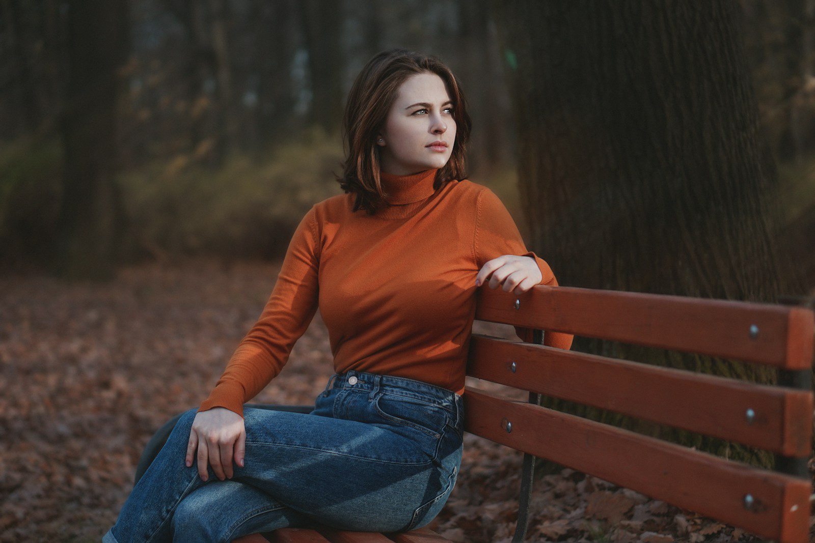 woman in red long sleeve shirt and blue denim jeans sitting on brown wooden bench