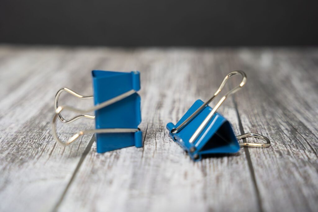 Close-up of blue binder clips on a textured wooden surface, showcasing office stationery essentials.