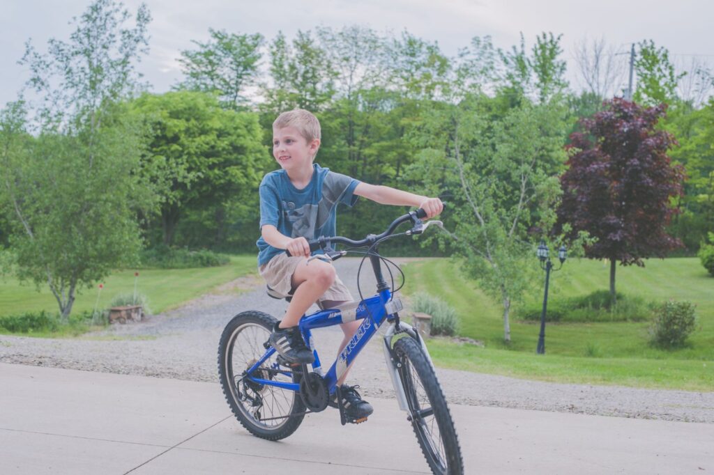 A young boy enjoys cycling outdoors in a lush green setting on a sunny day.