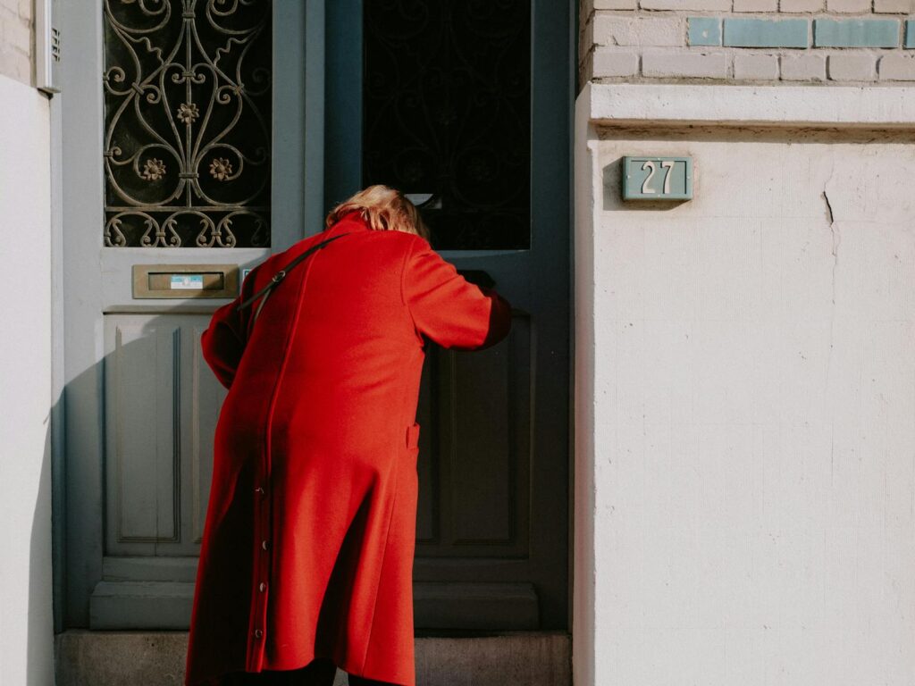 A person in a red coat enters a distinctive blue door with ornate decoration.