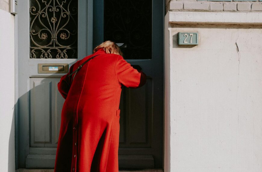 A person in a red coat enters a distinctive blue door with ornate decoration.