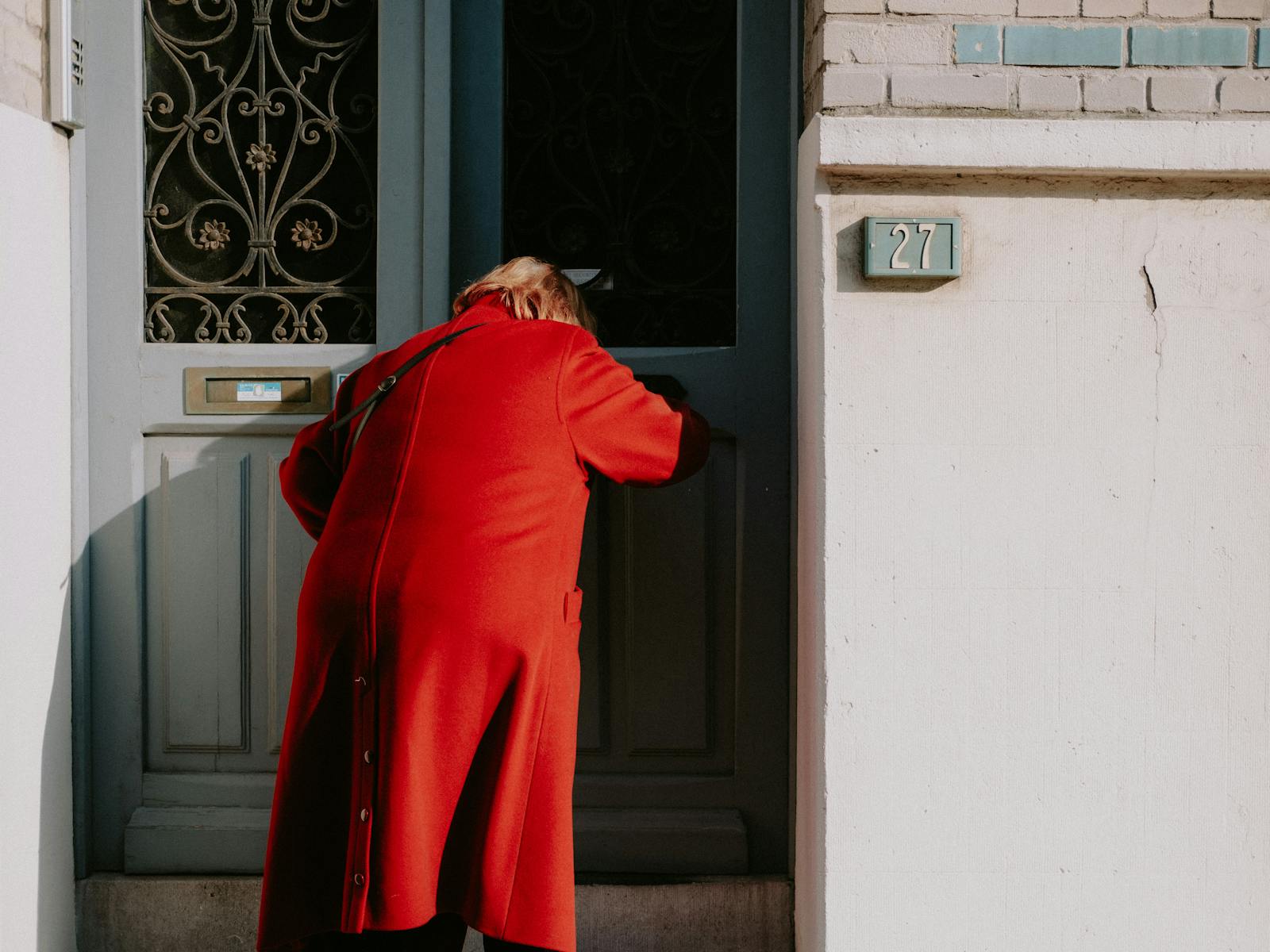 A person in a red coat enters a distinctive blue door with ornate decoration.