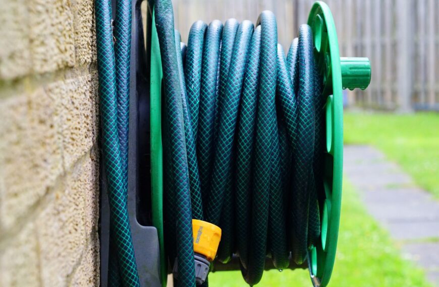 A neatly coiled garden hose on a wall-mounted reel against a brick wall.