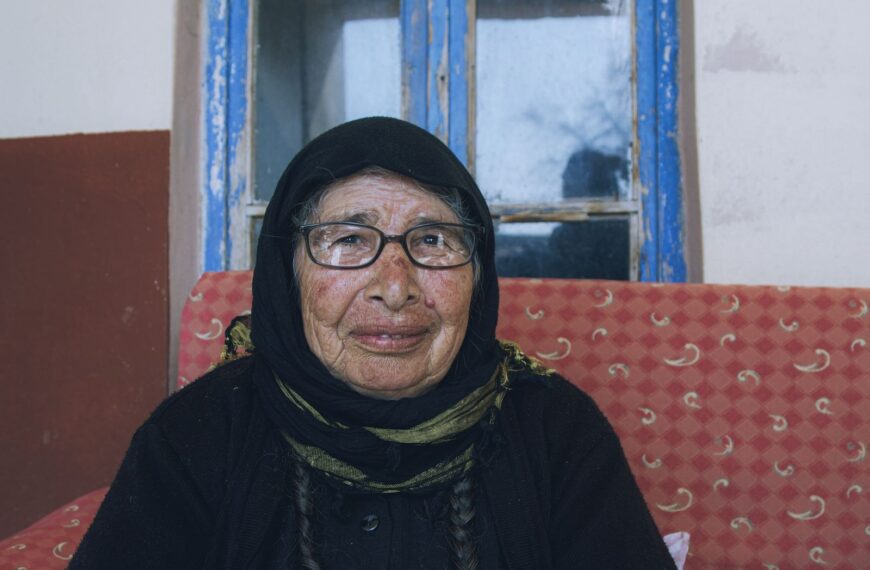 A warm portrait of an elderly woman with glasses in traditional clothing indoors.