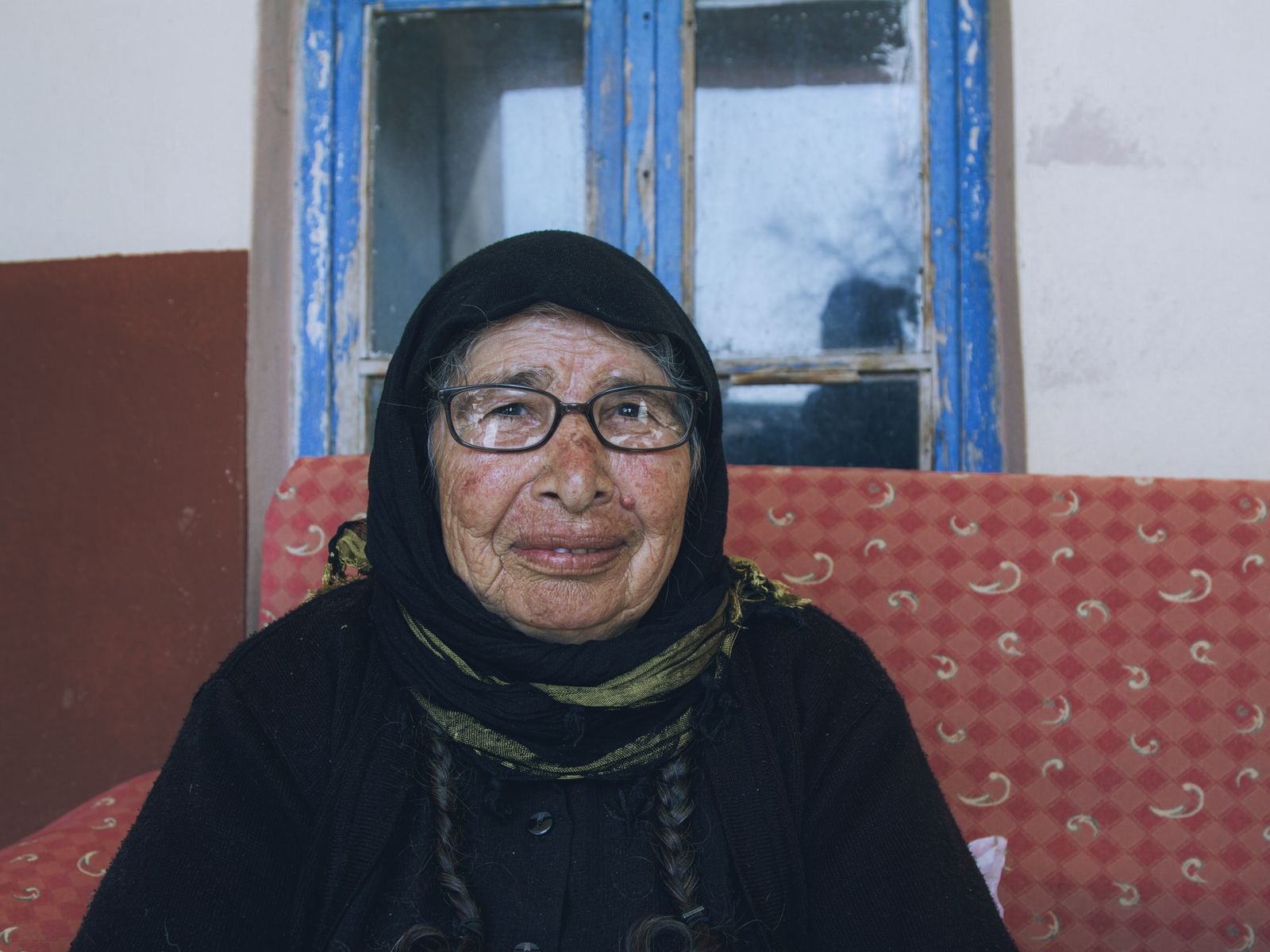 A warm portrait of an elderly woman with glasses in traditional clothing indoors.