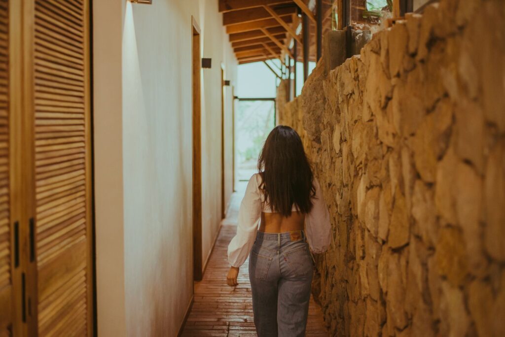 A young woman with long hair walks down a rustic corridor in casual style.