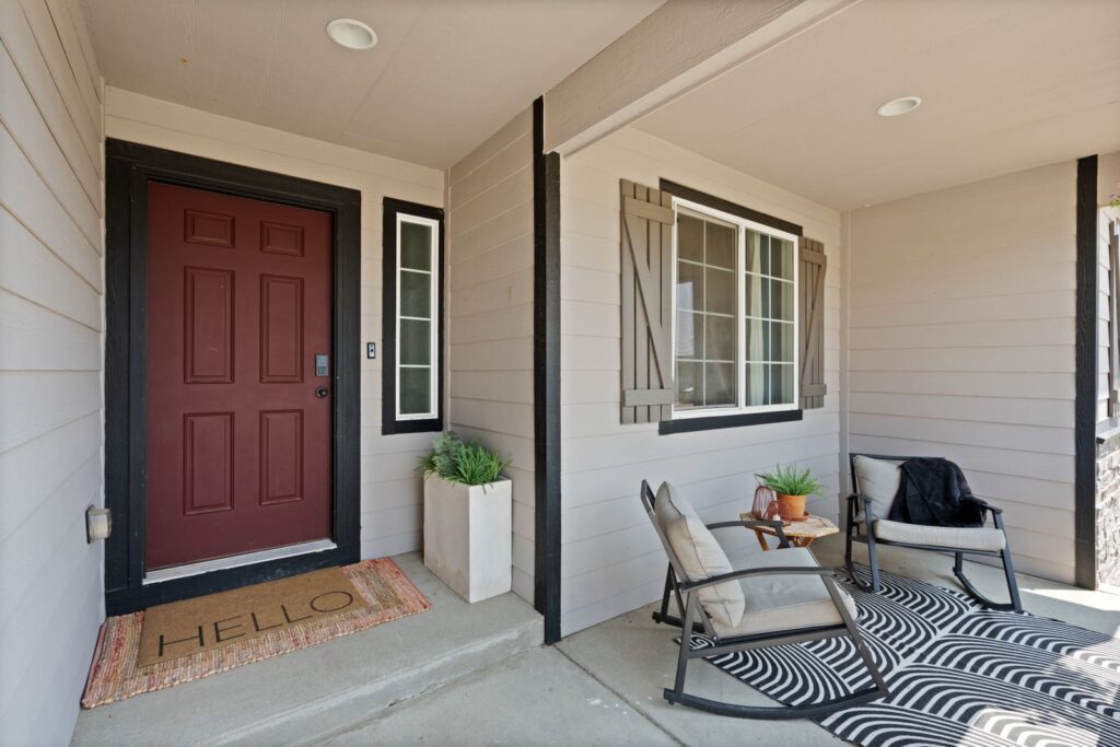 Inviting front porch featuring cozy chairs, a doormat, and plants.