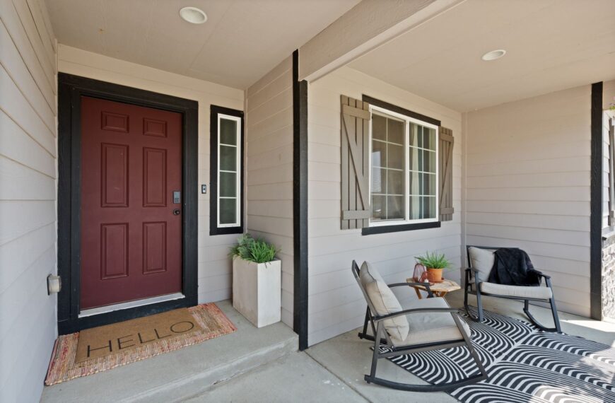 Inviting front porch featuring cozy chairs, a doormat, and plants.