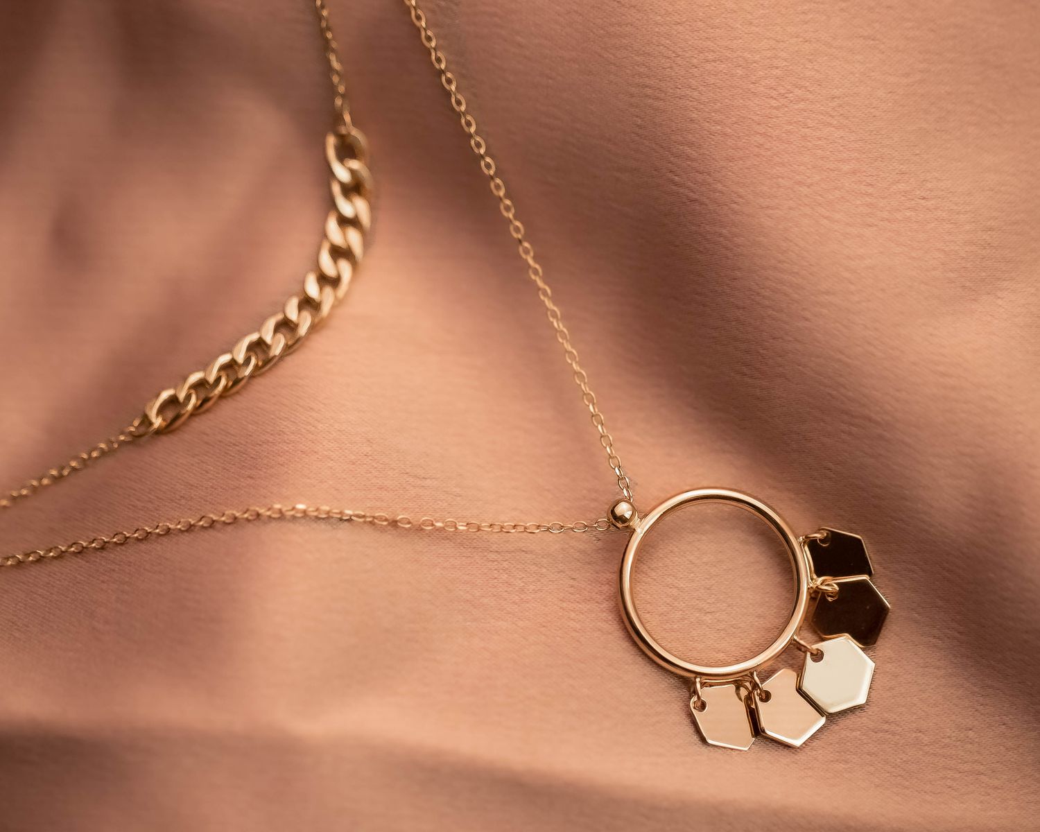 Close-up of a stylish gold necklace with hexagonal charms on textured fabric, showcasing elegance.