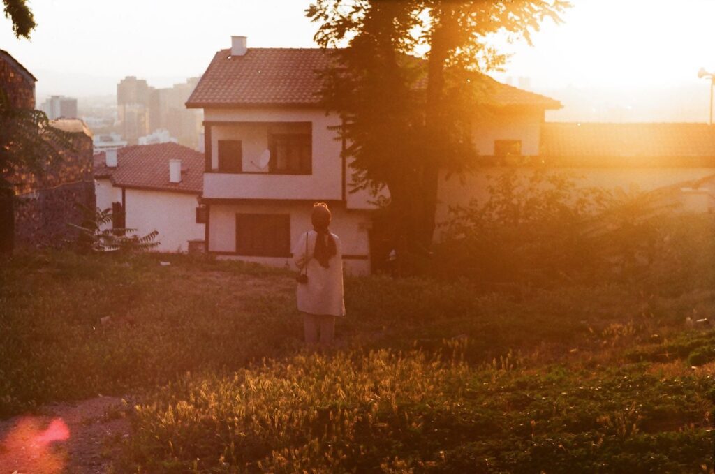 A woman stands in a yard facing a house during a captivating twilight scene.