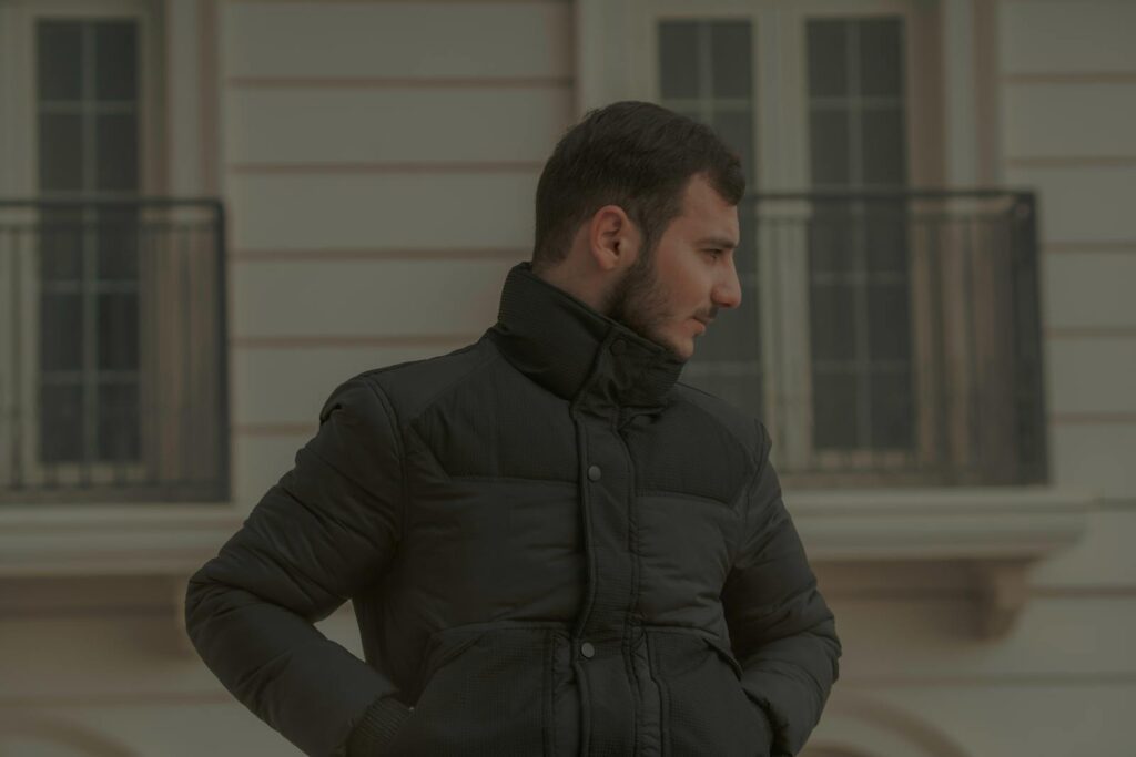 Portrait of a man in a black jacket standing outdoors against an urban background.