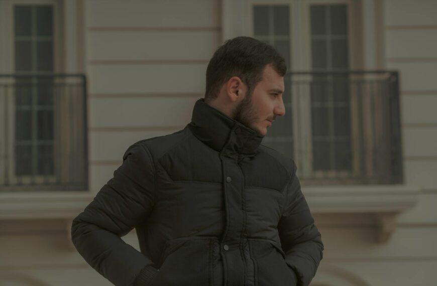 Portrait of a man in a black jacket standing outdoors against an urban background.