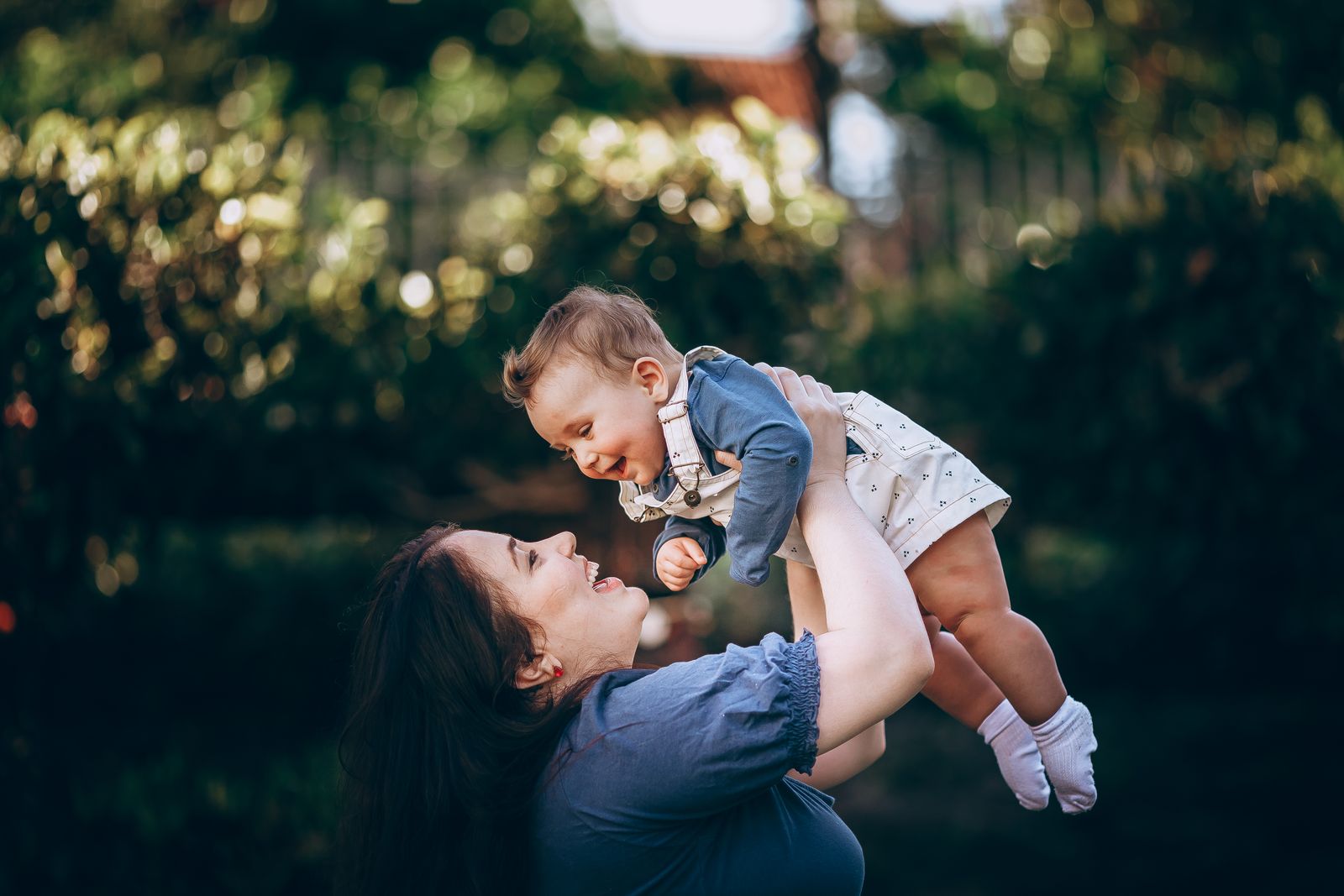 A joyful mother lifts her smiling baby outdoors in a summer park, capturing a loving moment.