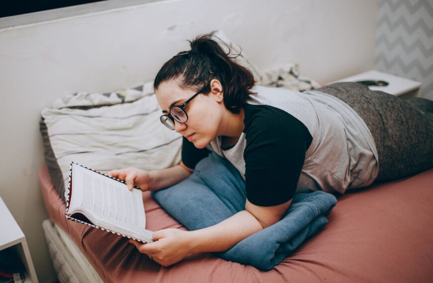 A woman is comfortably lying in bed reading a book, enjoying a peaceful moment.