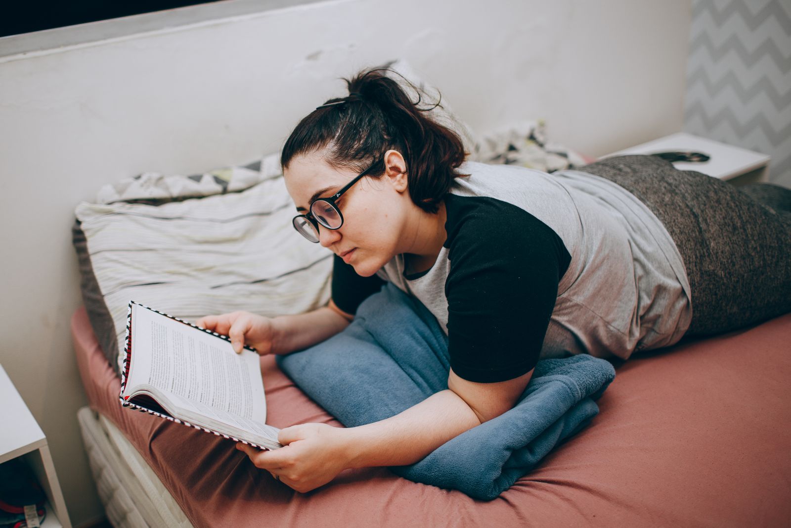 A woman is comfortably lying in bed reading a book, enjoying a peaceful moment.