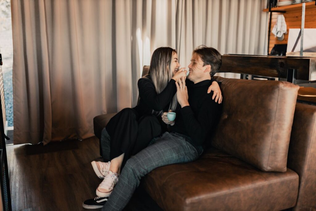 A happy couple laughing and enjoying coffee together on a cozy indoor sofa setting.