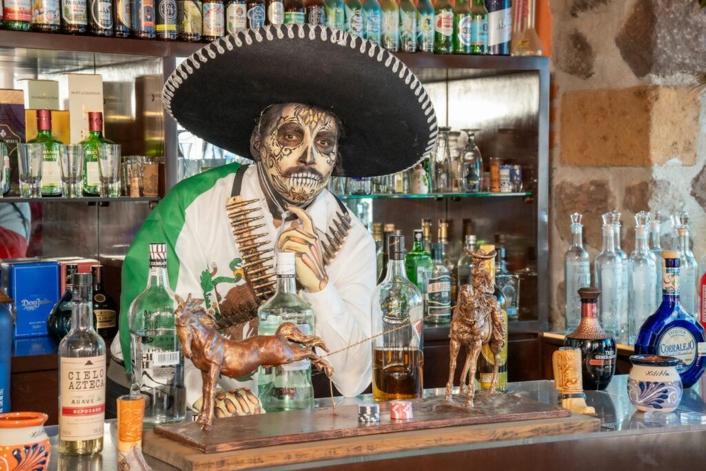 La Catrina themed bartender in traditional attire serving drinks at Mexican bar.