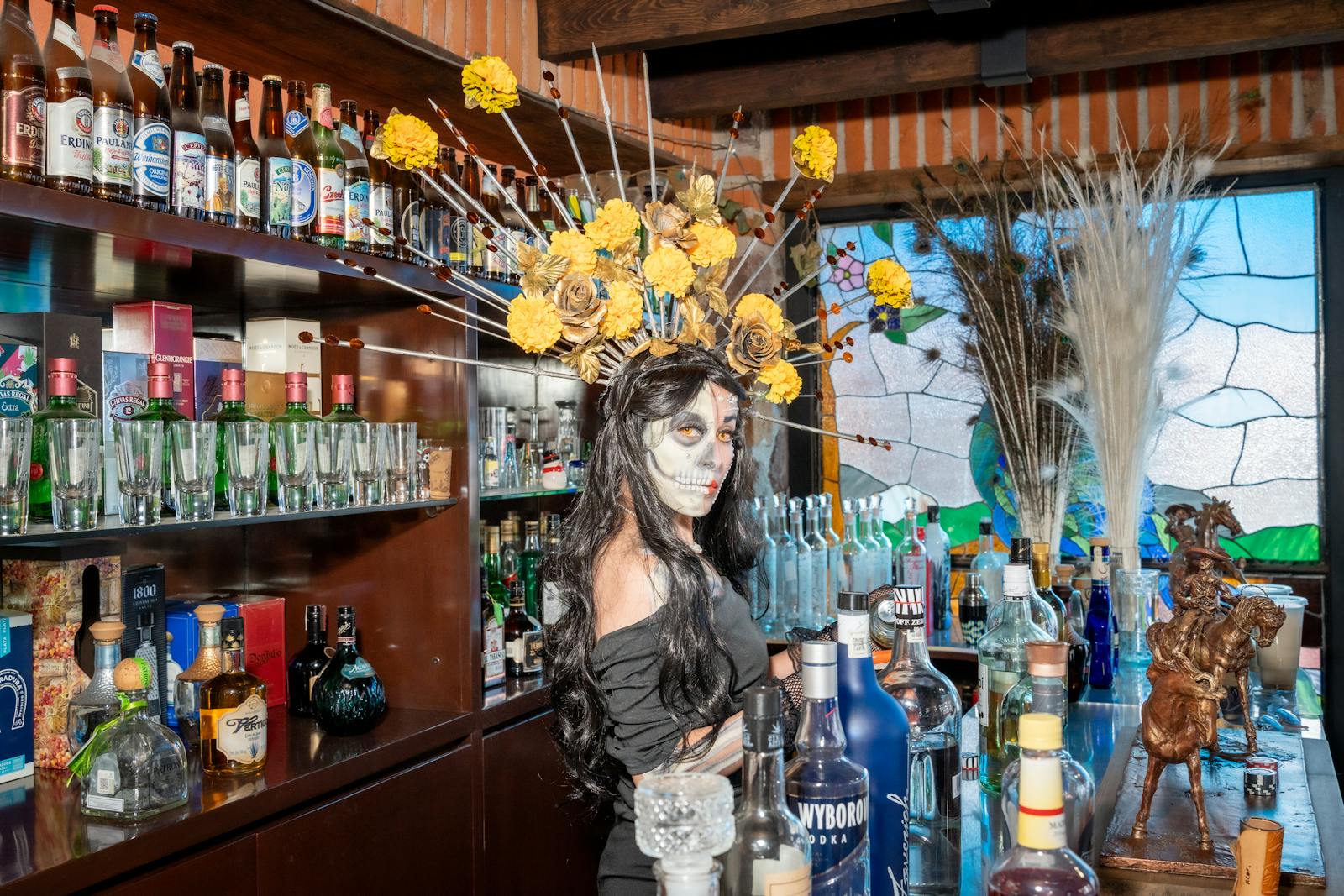 A woman in Dia de los Muertos makeup stands in a vibrant Mexico City bar.