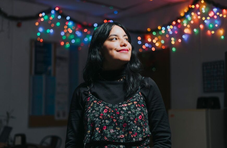 Portrait of a smiling young woman in a room adorned with colorful festive lights.