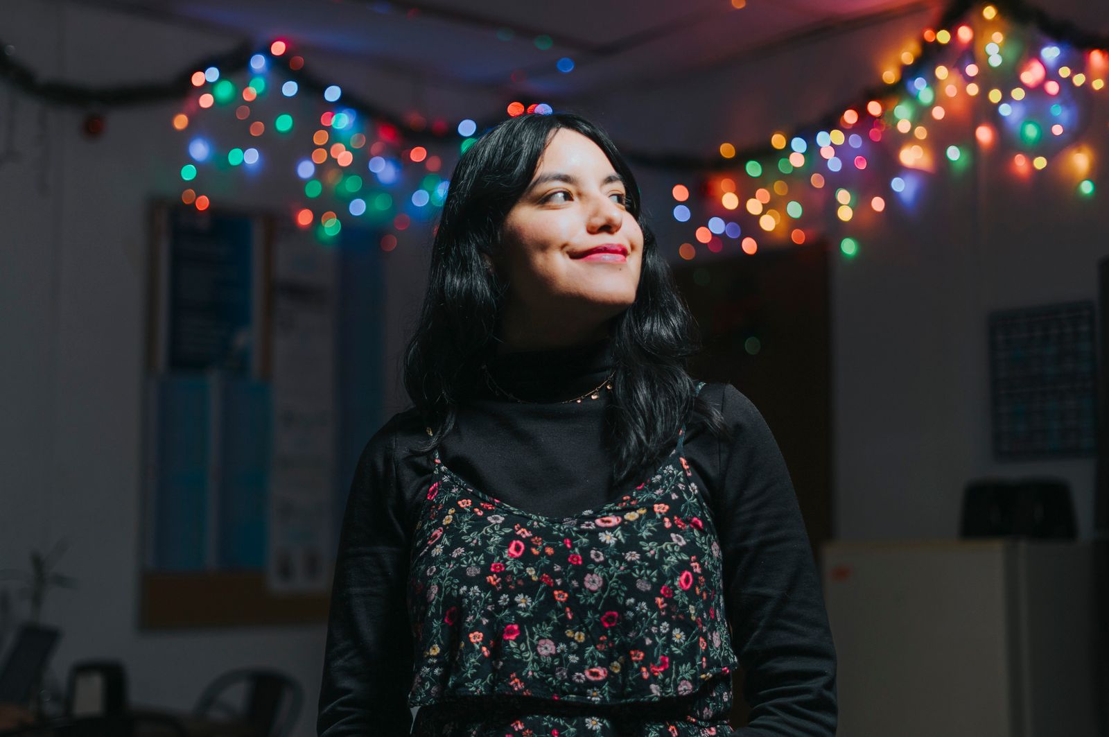 Portrait of a smiling young woman in a room adorned with colorful festive lights.