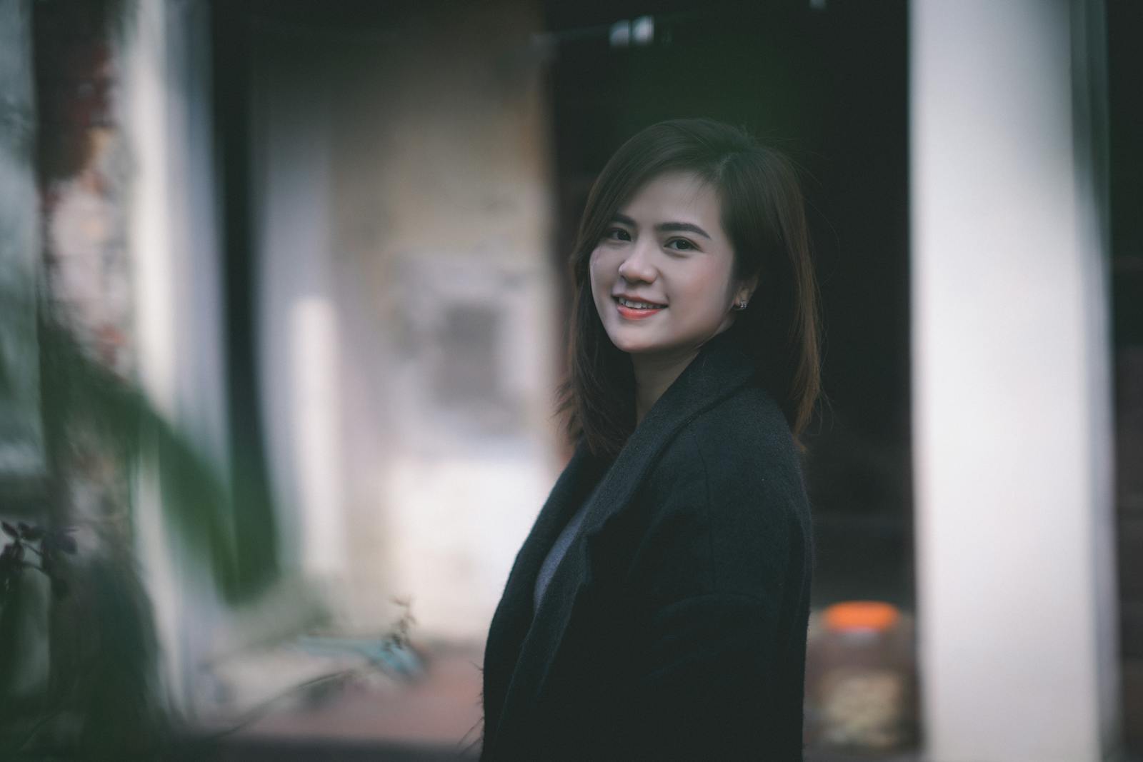 A woman stands outdoors, smiling warmly, in a black coat.