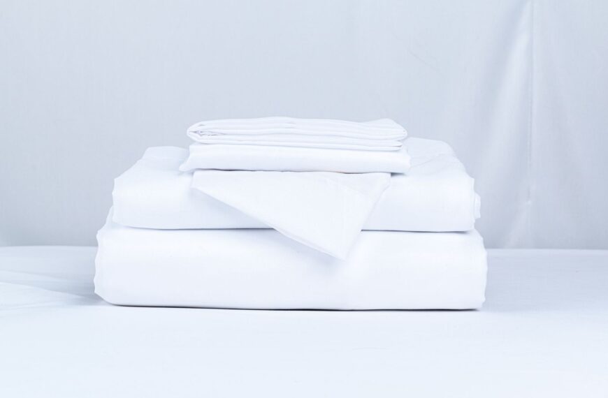 A neatly folded stack of crisp white bed linens on a clean surface.