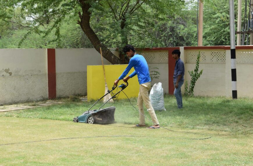 Young men working together on lawn maintenance with a mower in a sunny garden setting.