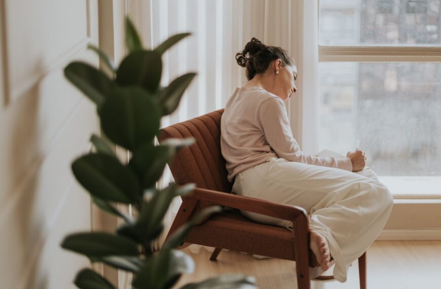 Woman relaxing on a chair by a window, deep in thought, indoors.