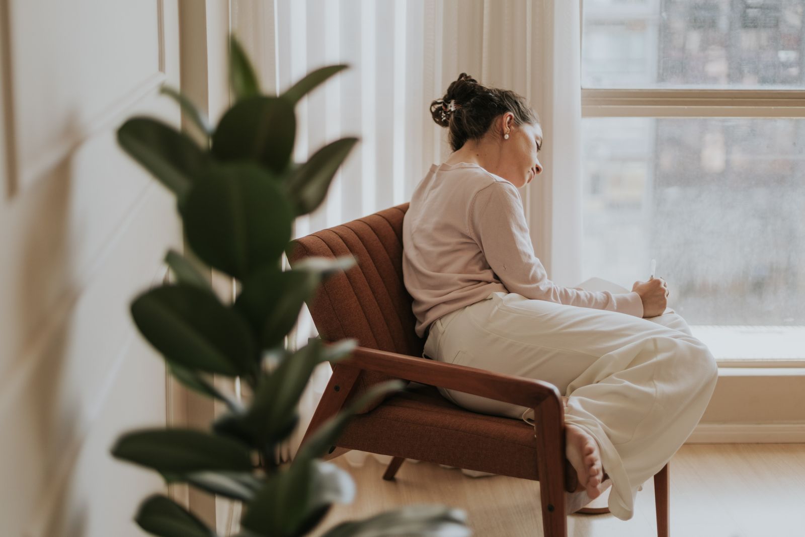 Woman relaxing on a chair by a window, deep in thought, indoors.