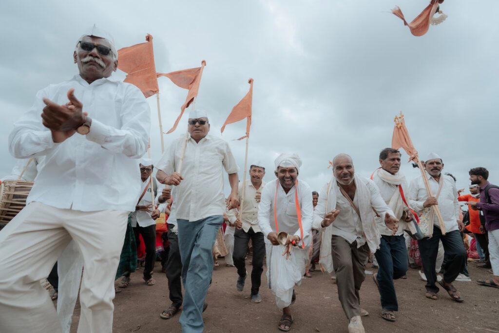 Vibrant outdoor group of Indian men celebrating with orange flags under a cloudy sky.