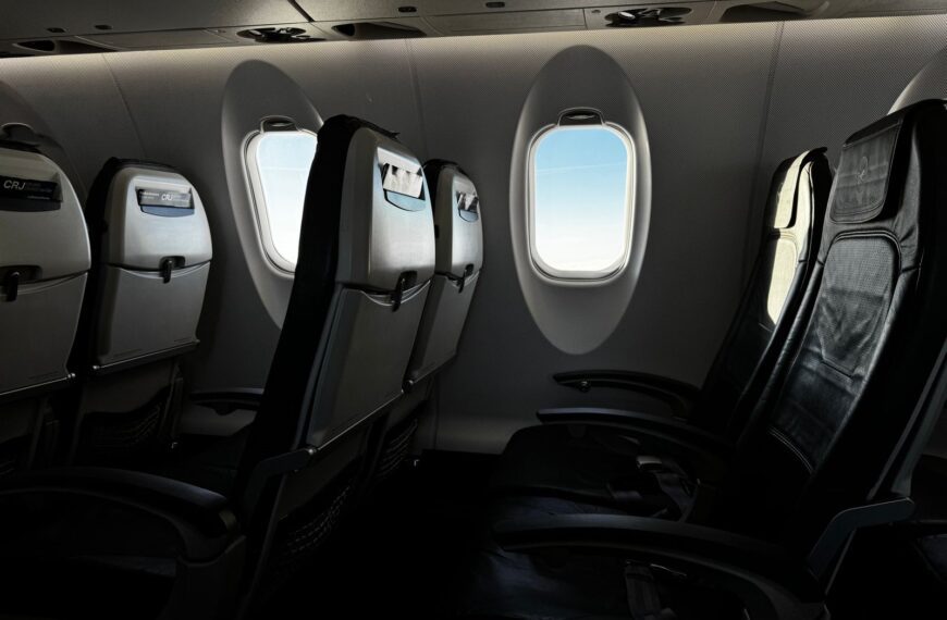 Interior of an empty airplane cabin with a bright sky visible through the window.