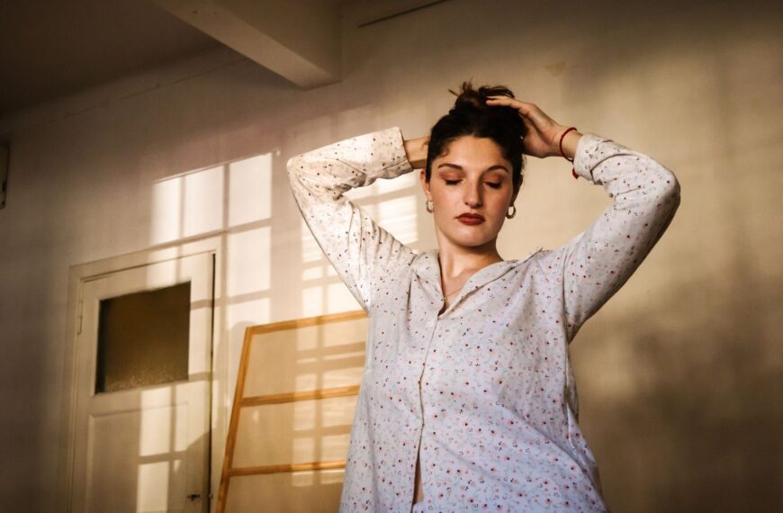 A woman stands with eyes closed in a sunlit room, exuding calm and peace.