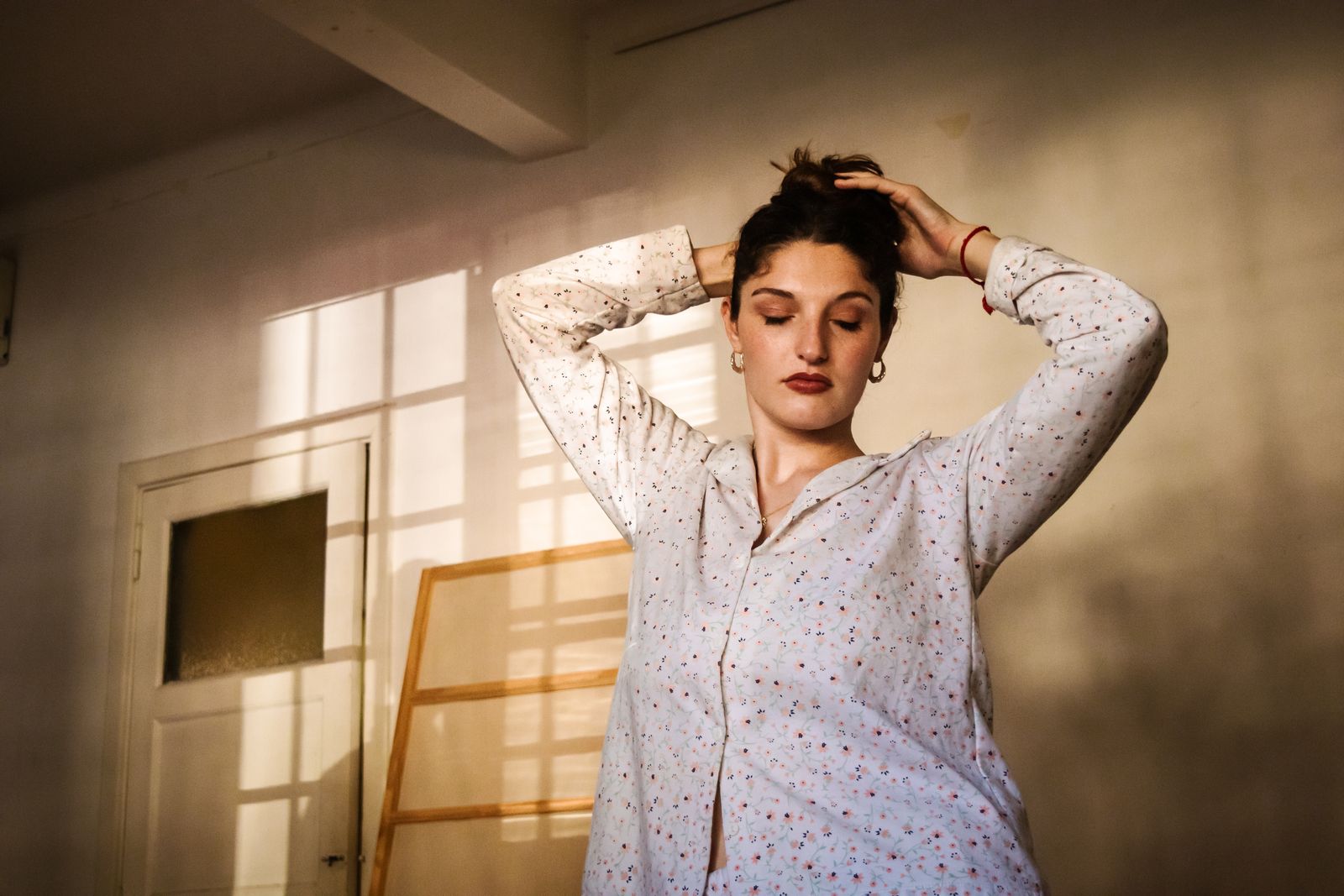 A woman stands with eyes closed in a sunlit room, exuding calm and peace.