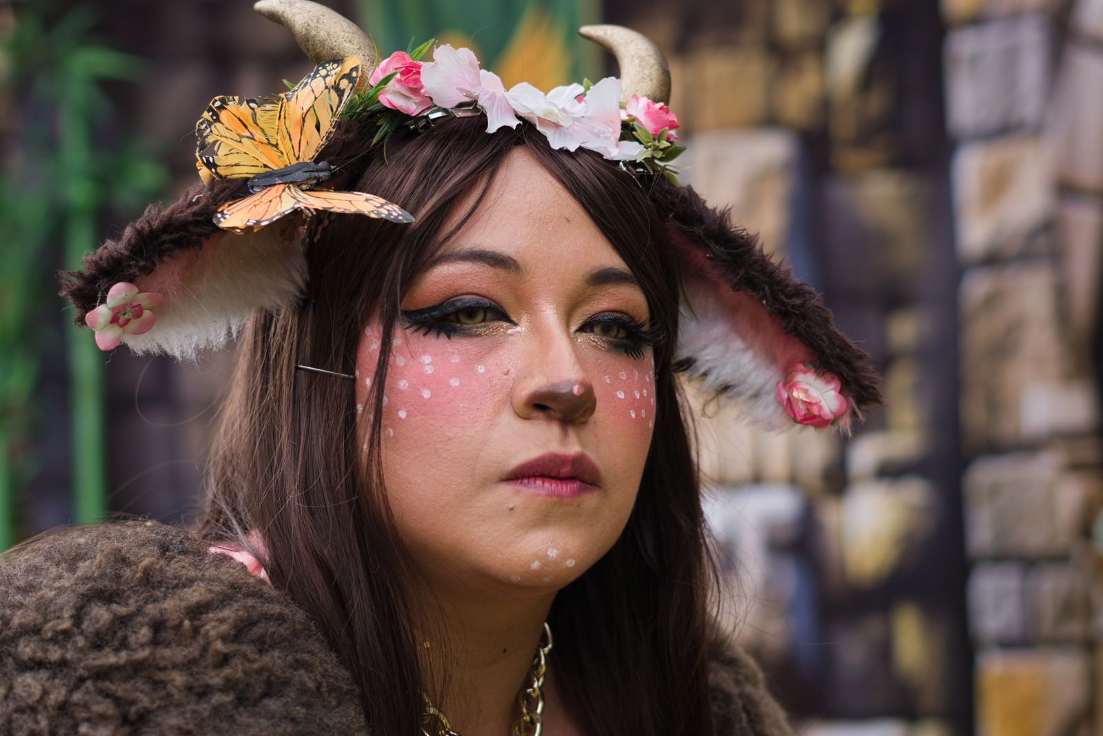 A close-up portrait of a person in a fantasy costume with horns, flowers, and a butterfly.
