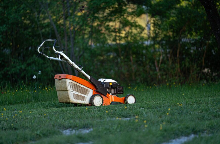 A lawn mower sits on a green lawn in a backyard, ready for yard work.