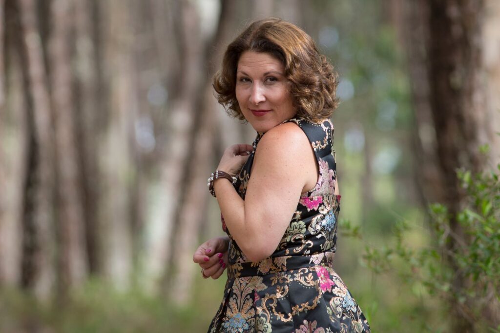 Woman in a stylish floral dress poses in a serene forest setting, capturing a moment of elegance.