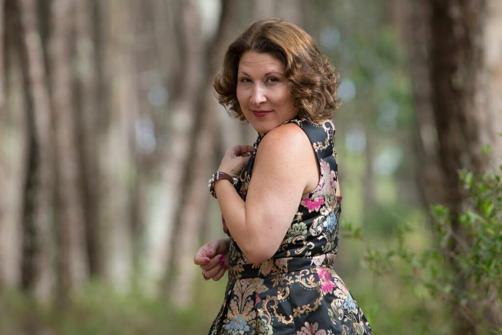 Woman in a stylish floral dress poses in a serene forest setting, capturing a moment of elegance.