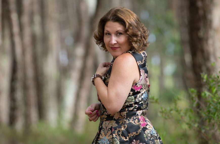 Woman in a stylish floral dress poses in a serene forest setting, capturing a moment of elegance.