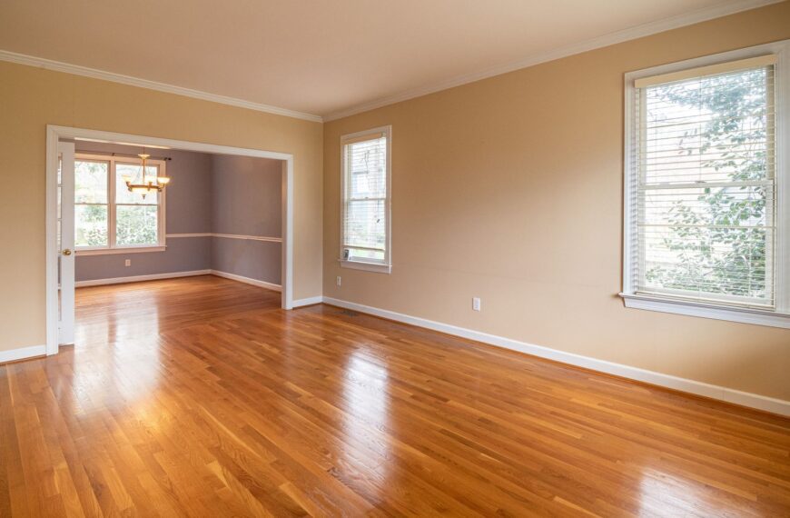 Bright empty room with wooden floors and large windows, ideal for real estate listings.