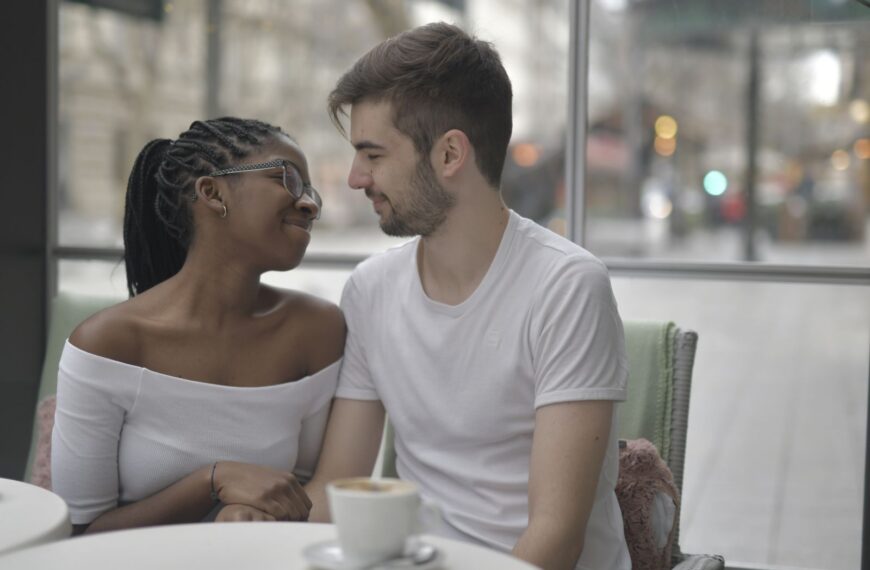 A loving multiracial couple shares a joyful moment over coffee, embracing affection and diversity indoors.