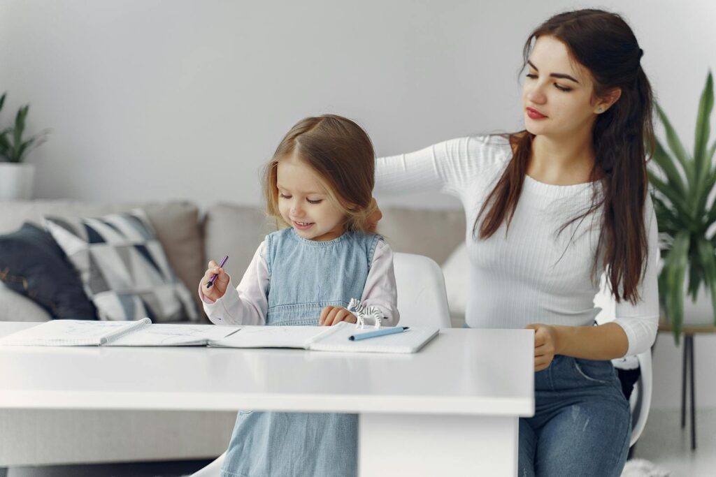 A loving mother helps her daughter with homework at home, fostering a nurturing learning environment.