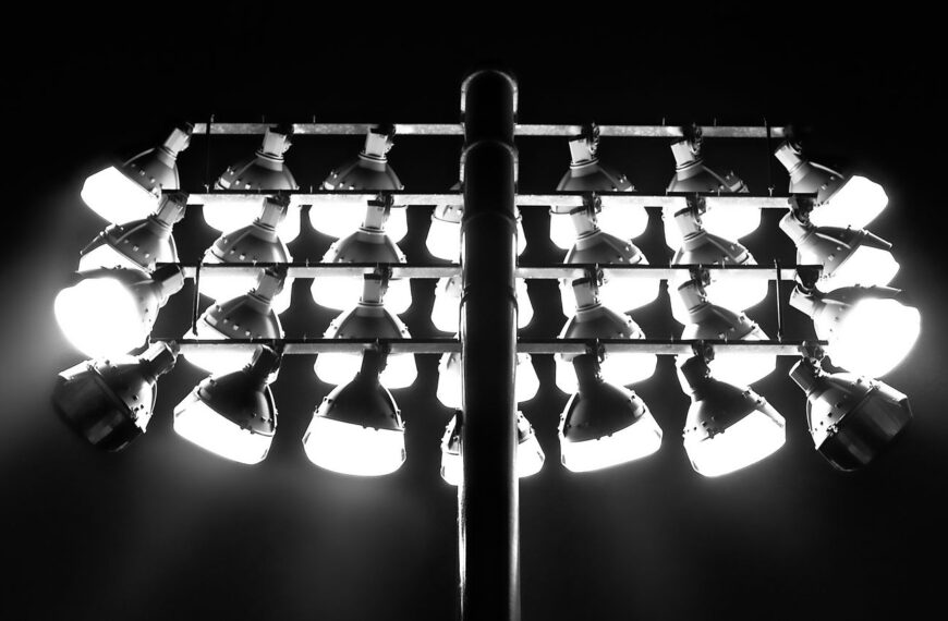 Monochrome image of illuminated floodlights against a dark nighttime sky.