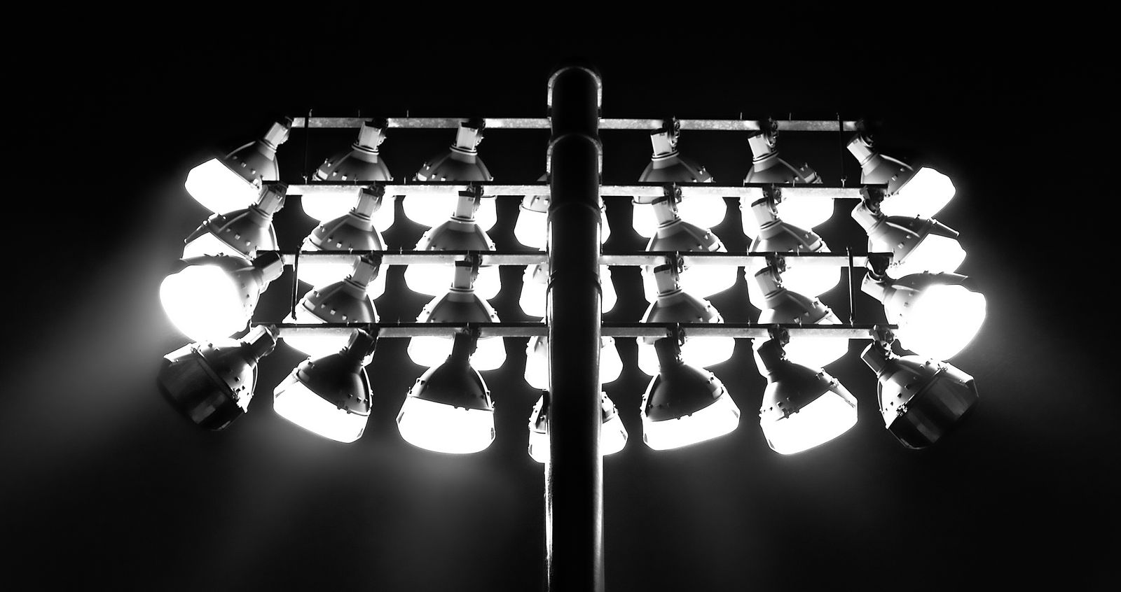 Monochrome image of illuminated floodlights against a dark nighttime sky.