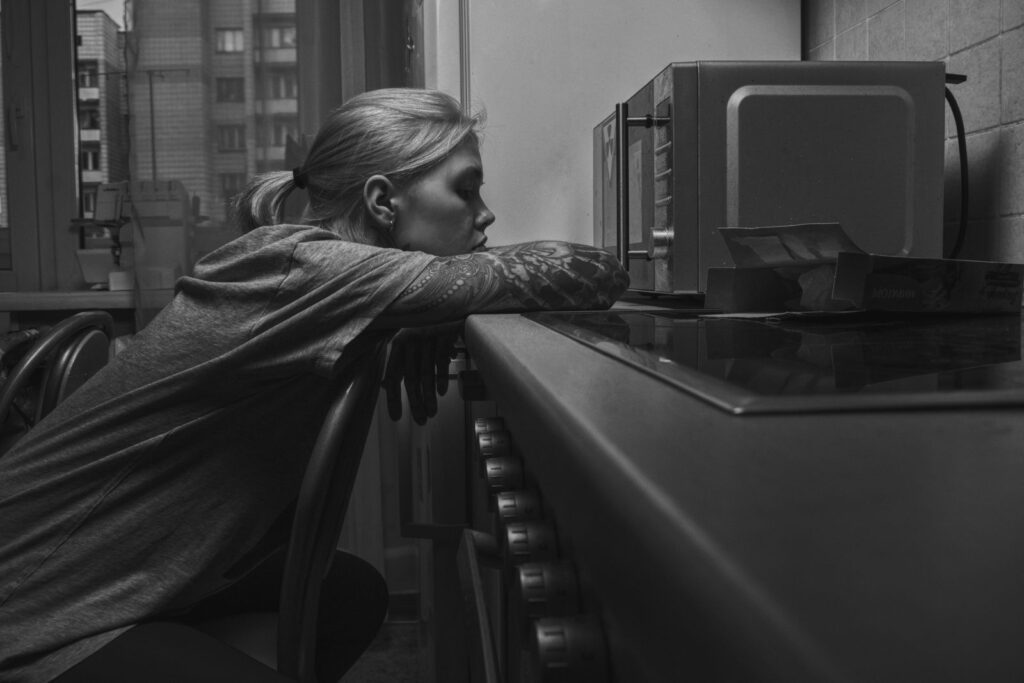 Woman in monochrome setting, resting on chair near a microwave, capturing a moment of reflection.