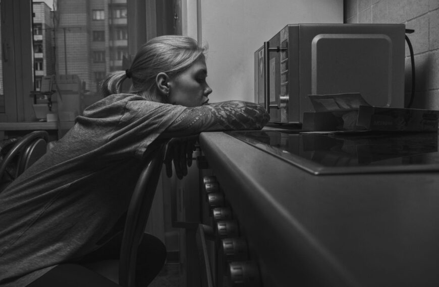 Woman in monochrome setting, resting on chair near a microwave, capturing a moment of reflection.